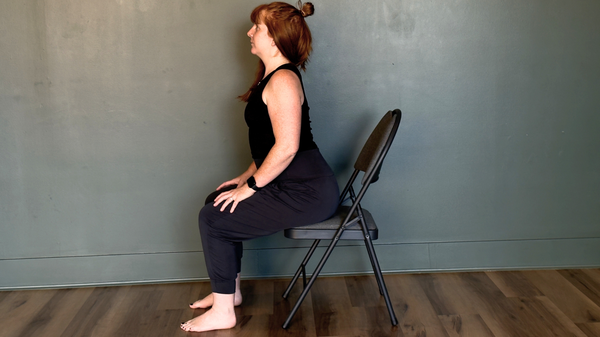 woman performing cat cow seated on a wooden floor against a sage green wall 