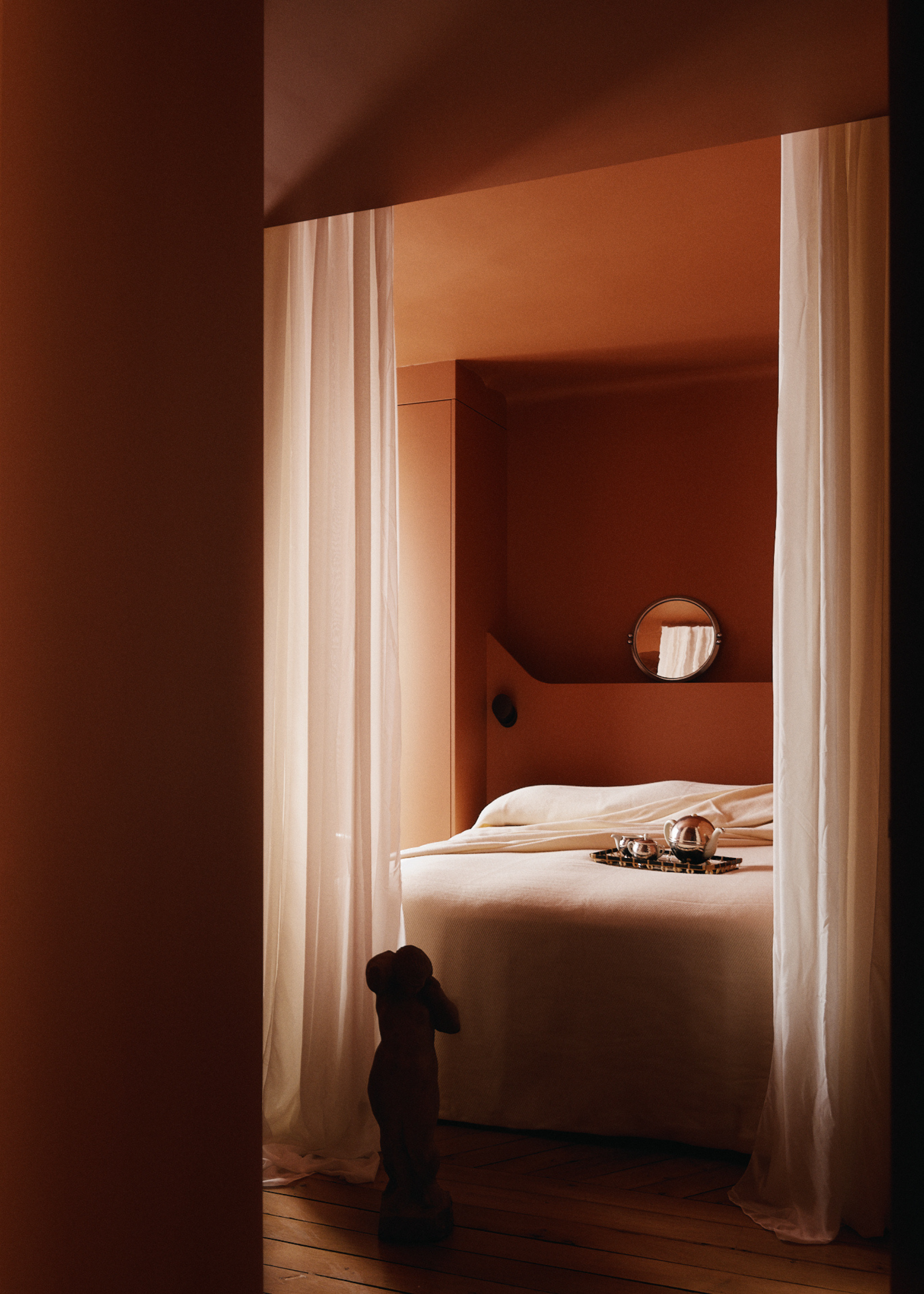 A soft pink bedroom with wispy curtains leading to a bed with a chrome tea set on a tray