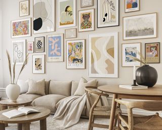 A beige sofa in living room with round small wooden dining table and gallery with framed wall art decor