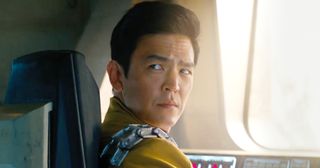 John Cho as Sulu in Star Trek: Into Darkness sitting at the comms. He had a metal bandolier against his yellow uniform. 