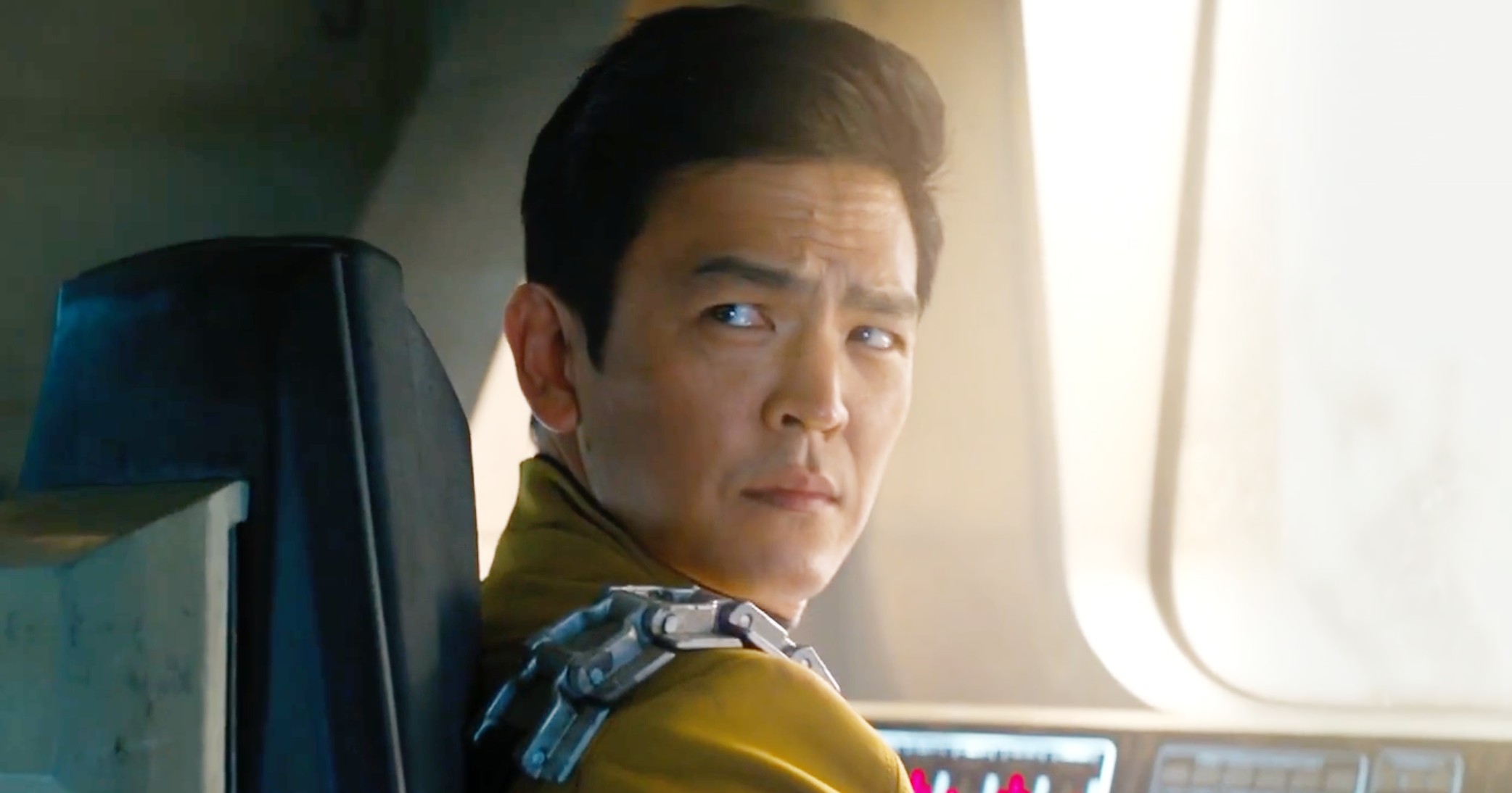 John Cho as Sulu in Star Trek: Into Darkness sitting at the comms. He had a metal bandolier against his yellow uniform. 