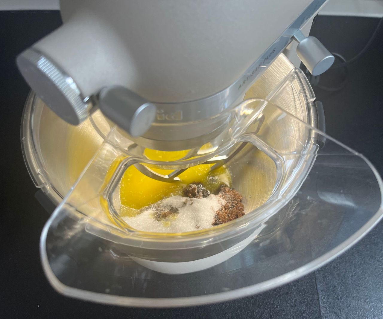A top down view of butter and sugar in a stainless steel mixing bowl, through a pouring spout
