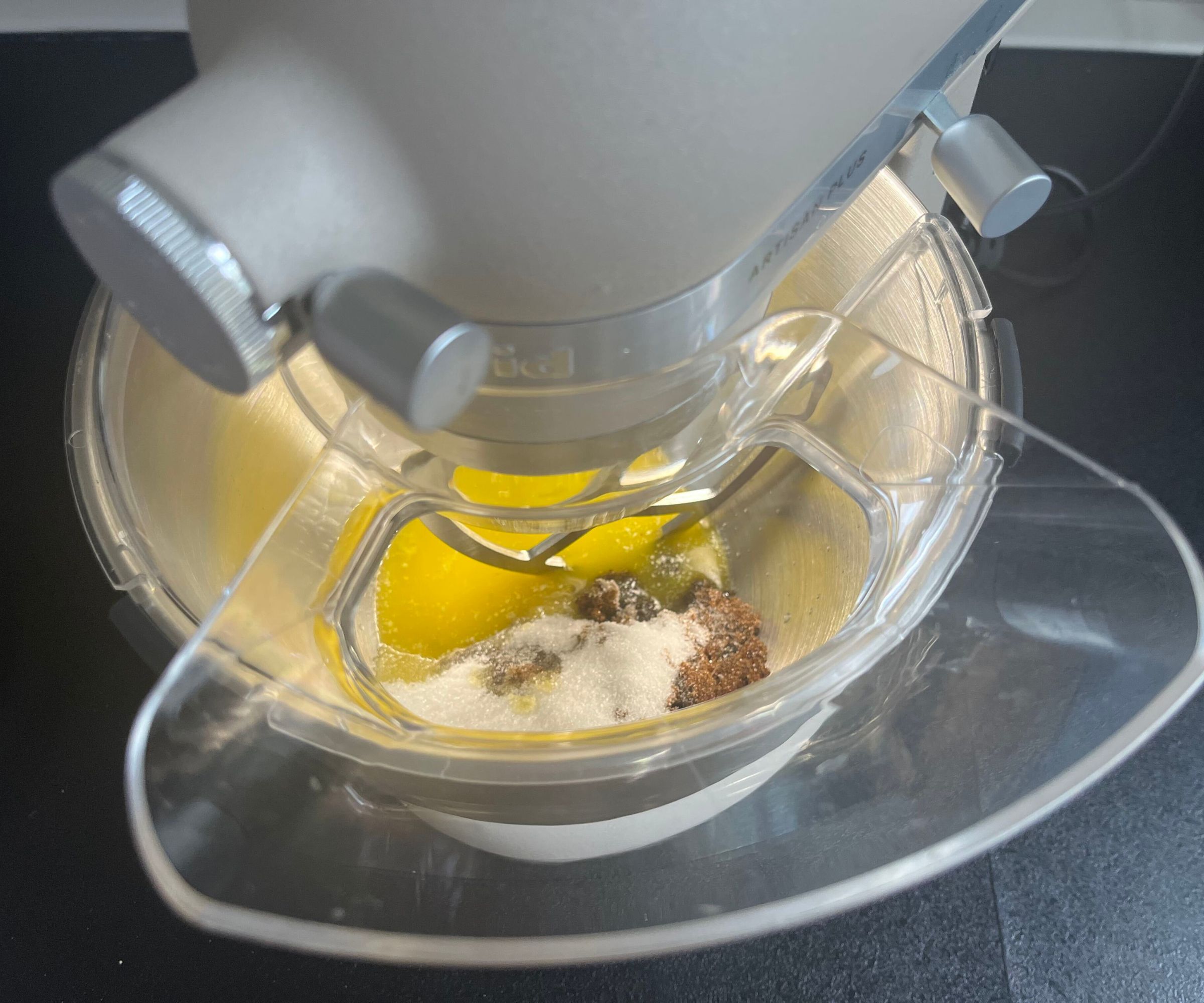 A top down view of butter and sugar in a stainless steel mixing bowl, through a pouring spout