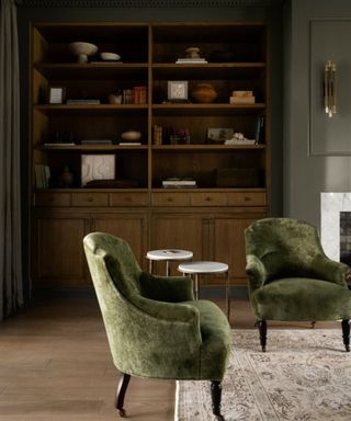 Green velvet armchairs in a green painted living room with dark wooden dresser