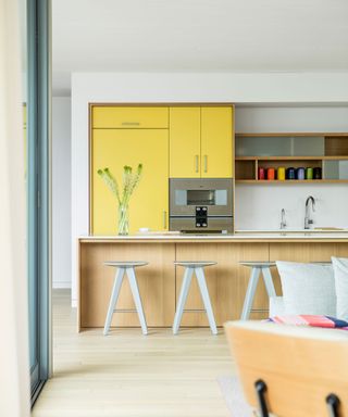 Modern yellow kitchen with wooden island and white stools