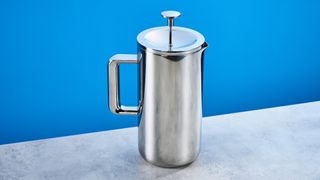 the aarke french press in silver showing the french press filter system, lid, spout, and inside photographed against the blue tom's guide background