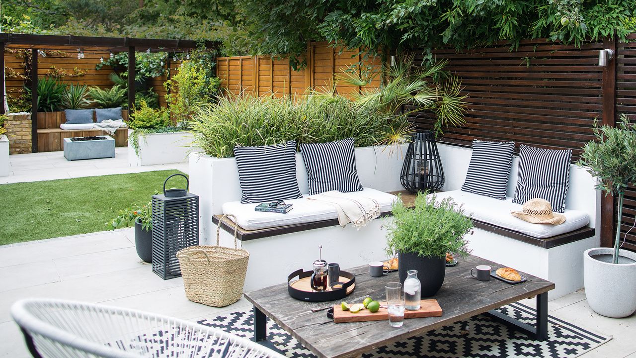 Garden with built-in L-shaped bench seating with white seat pads and black and white striped cushions