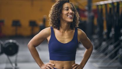Strong woman smiling in gym with hands on her hips