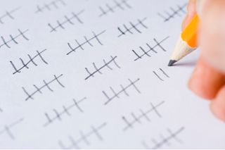 A white page covered with tallies marked in pencil with a close up of a tally line being marked