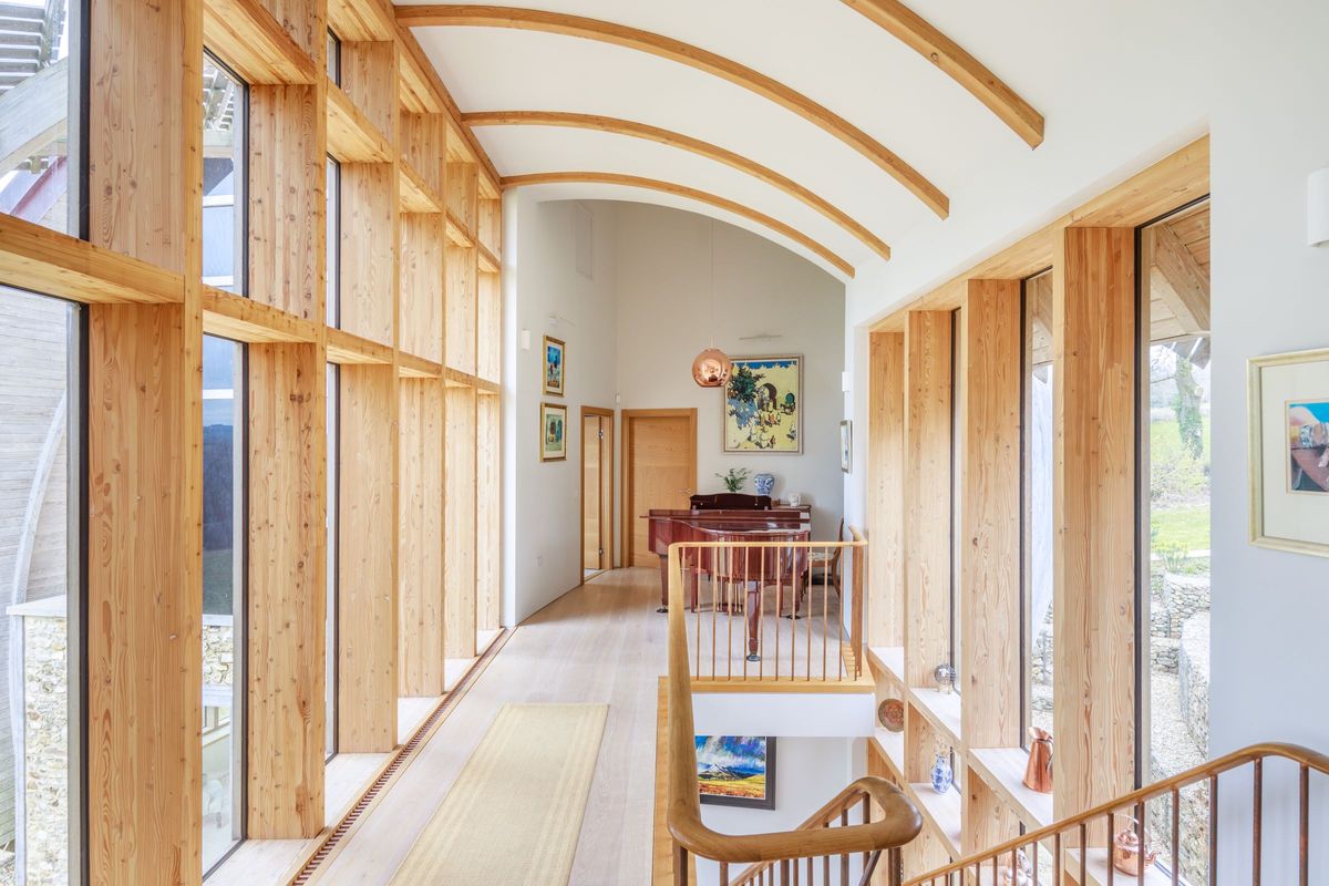 The top of the stairs shows a piano and woodne frame windows either side and a curved timber ceiling