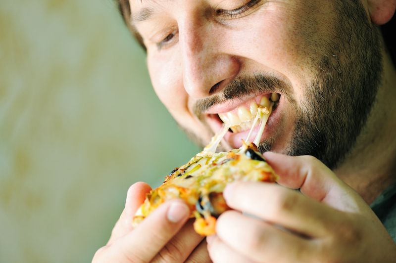 A man devours a piece of pizza.