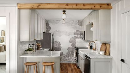 Hillcrest cottage by Joanna Gaines with light gray cabinets, marble countertops, a wallpaper mural, and wooden decor