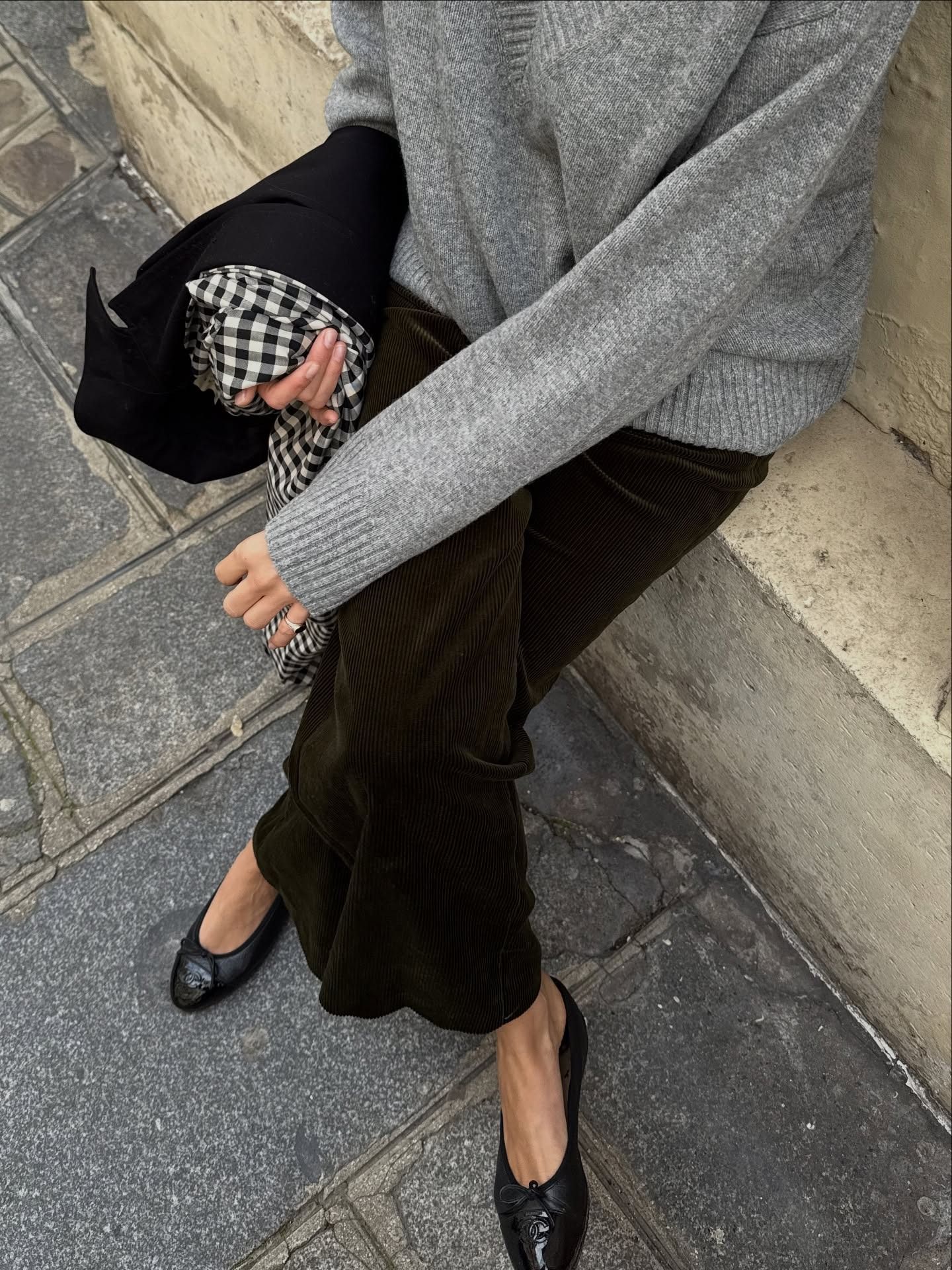 Influencer sits on a bench wearing corduroy trousers with black ballet flats and a grey jumper.