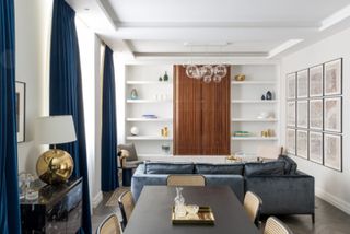 An open plan living / dining room with rattan chairs, a black dining table and blue velvet curtains in the windows