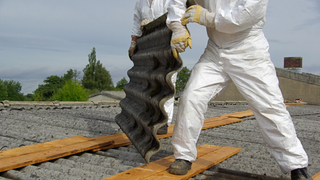 Two people wearing overalls lifting a roof tile off of a roof