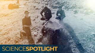 A photo of three men crouched around a hole in the ground emitting helium gas