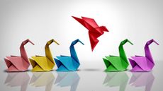 Origami bird in flight among a row of origami swans