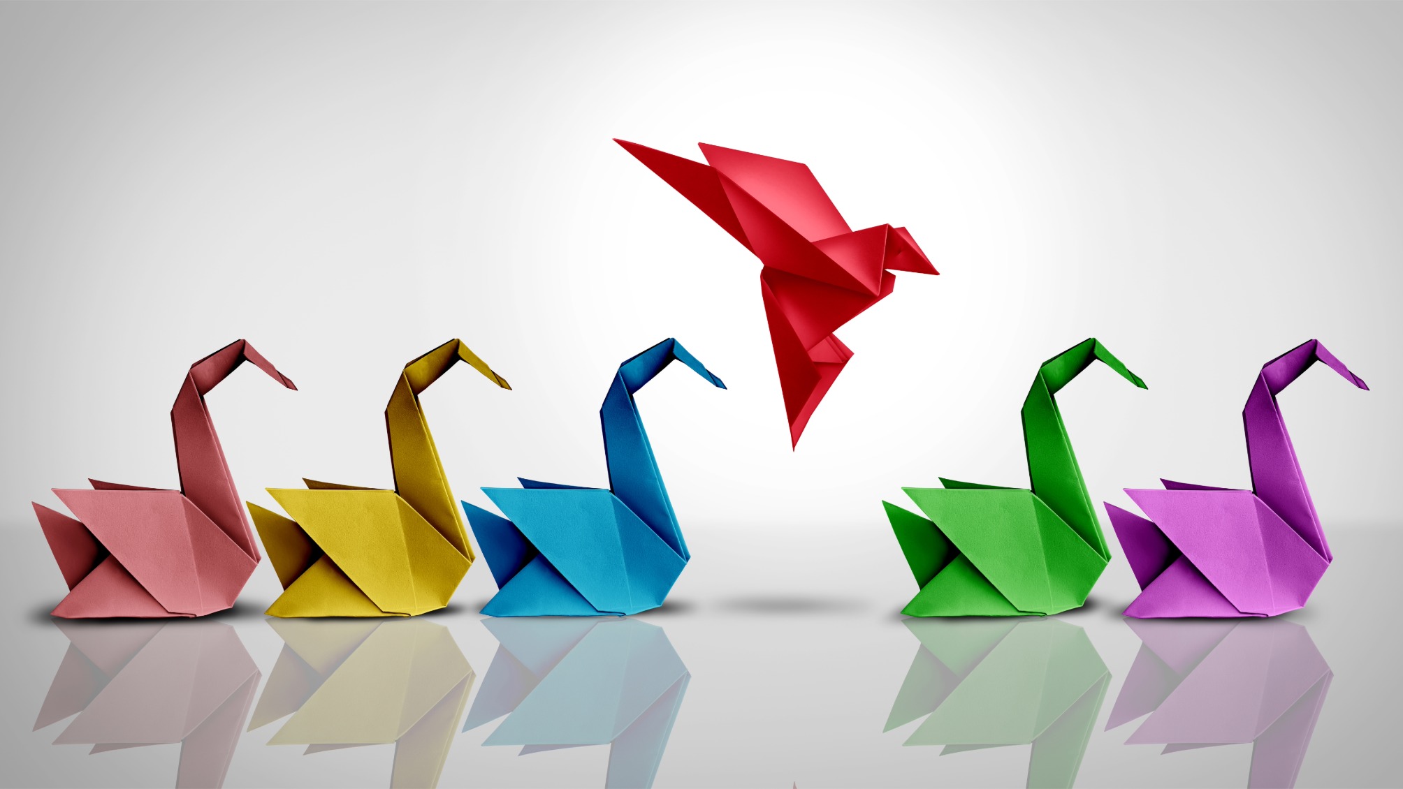 Origami bird in flight among a row of origami swans
