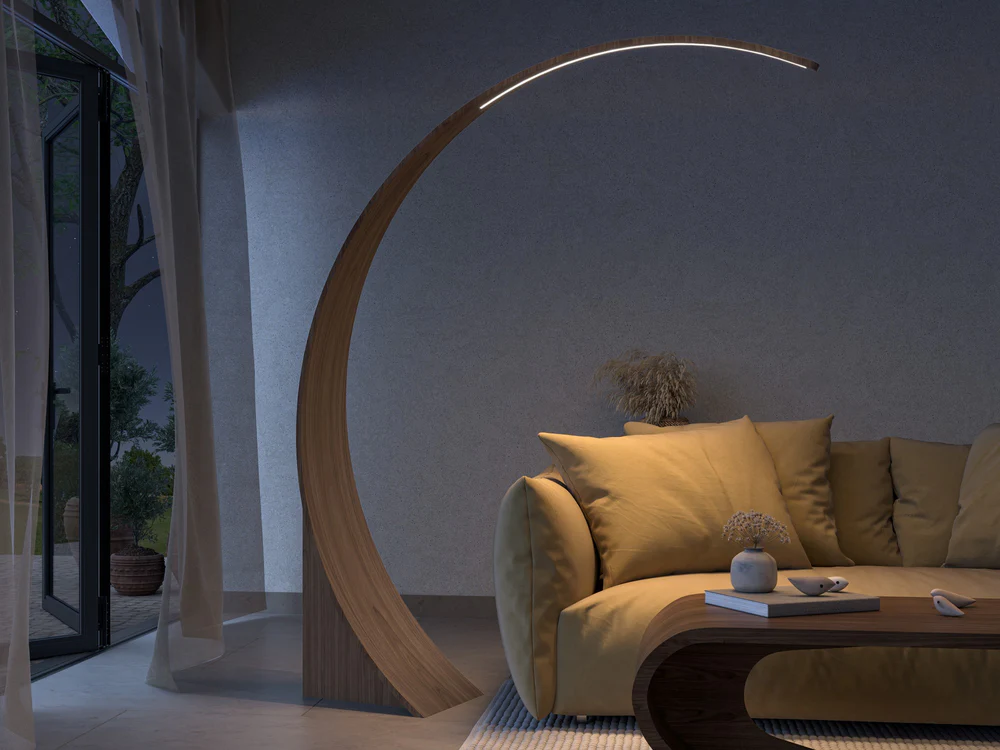large curved timber floor lamp leaning over sofa with large cushions, and a curved coffee table, with curtains covering doors leading to outside