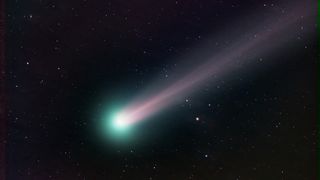 The comet appears to have a glowing green/blue nucleus and a long pink/white tail stretch off in one direction as it streaks across a star-studded sky. 