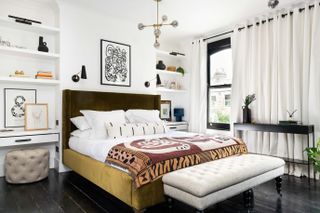 green and white bedroom with olive green bed, shelving, dressing tables, black floor, black wall lights, retro pendant light, footstool, artwork