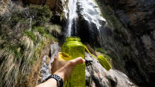 person filling up a bottle with water for hiking