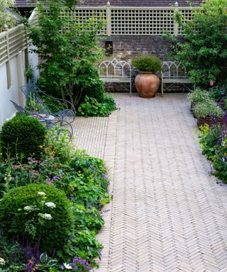 herringbone paving pattern in a narrow walled garden with gothic style metal benches in design by Butter Wakefield