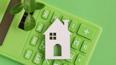 White house miniature and a leaf on top of a green calculator on a green background 
