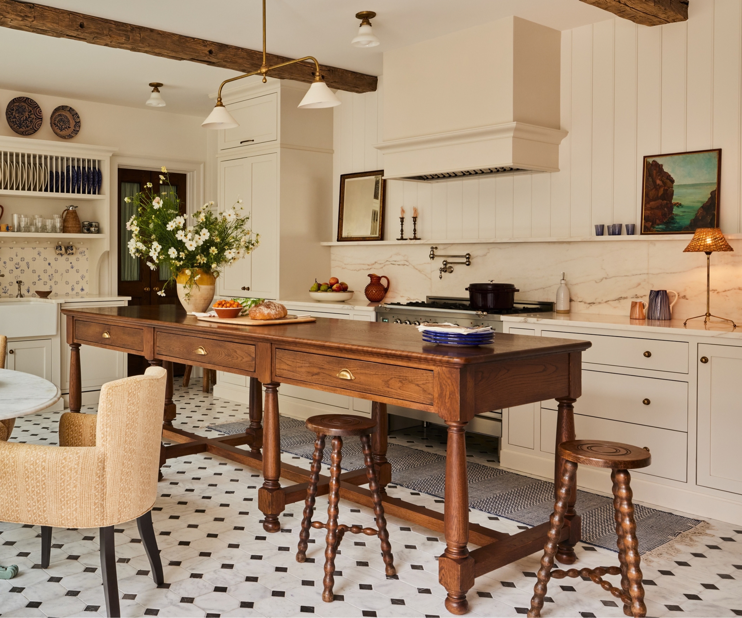 A warm neutral kitchen with a vintage freestanding wooden island with three drawers below the countertop and bobbin led wood stools surrounding it