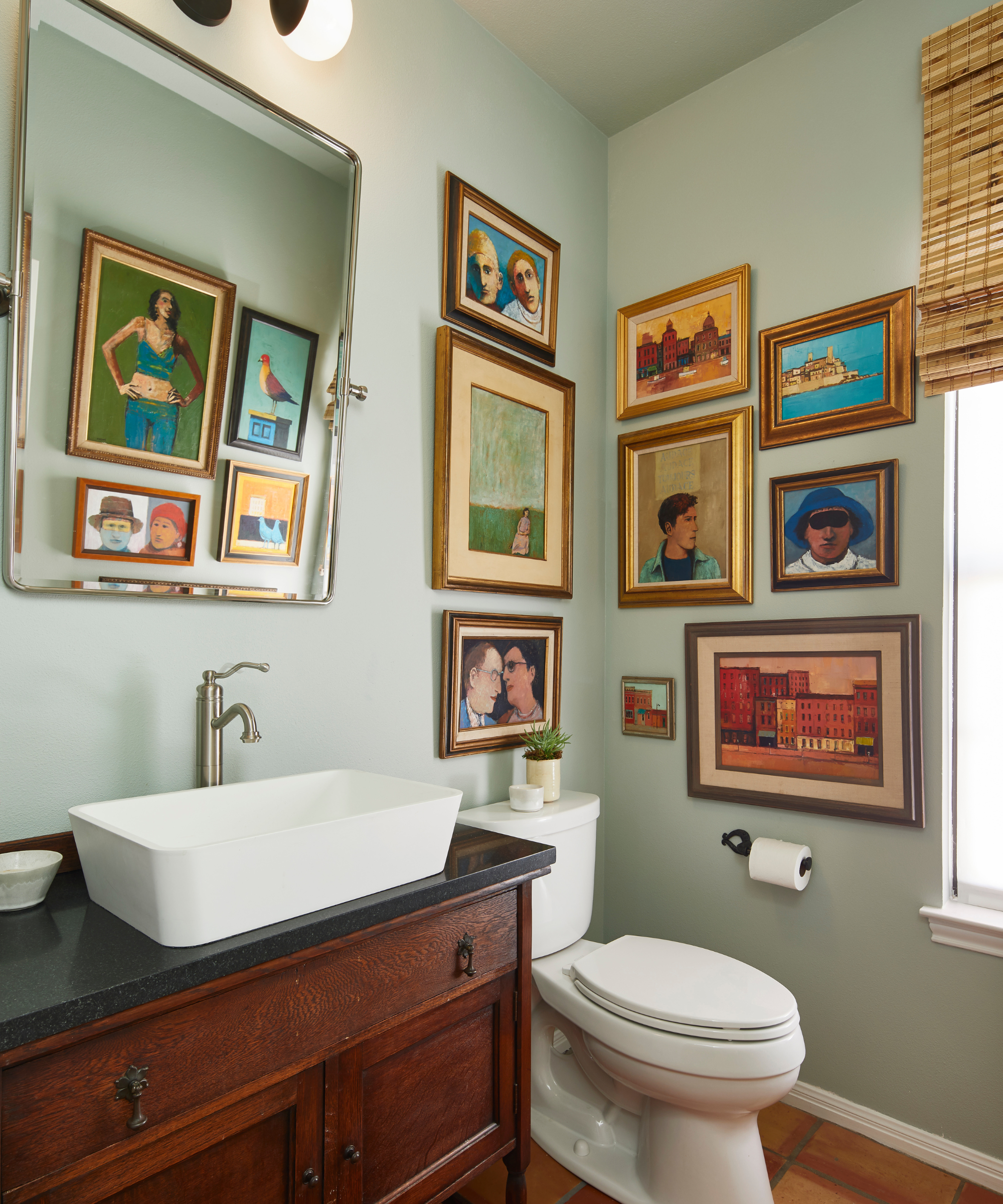 a bathroom with art hung in the corner, a white toilet, a white sink, and a wooden vanity with a black countertop