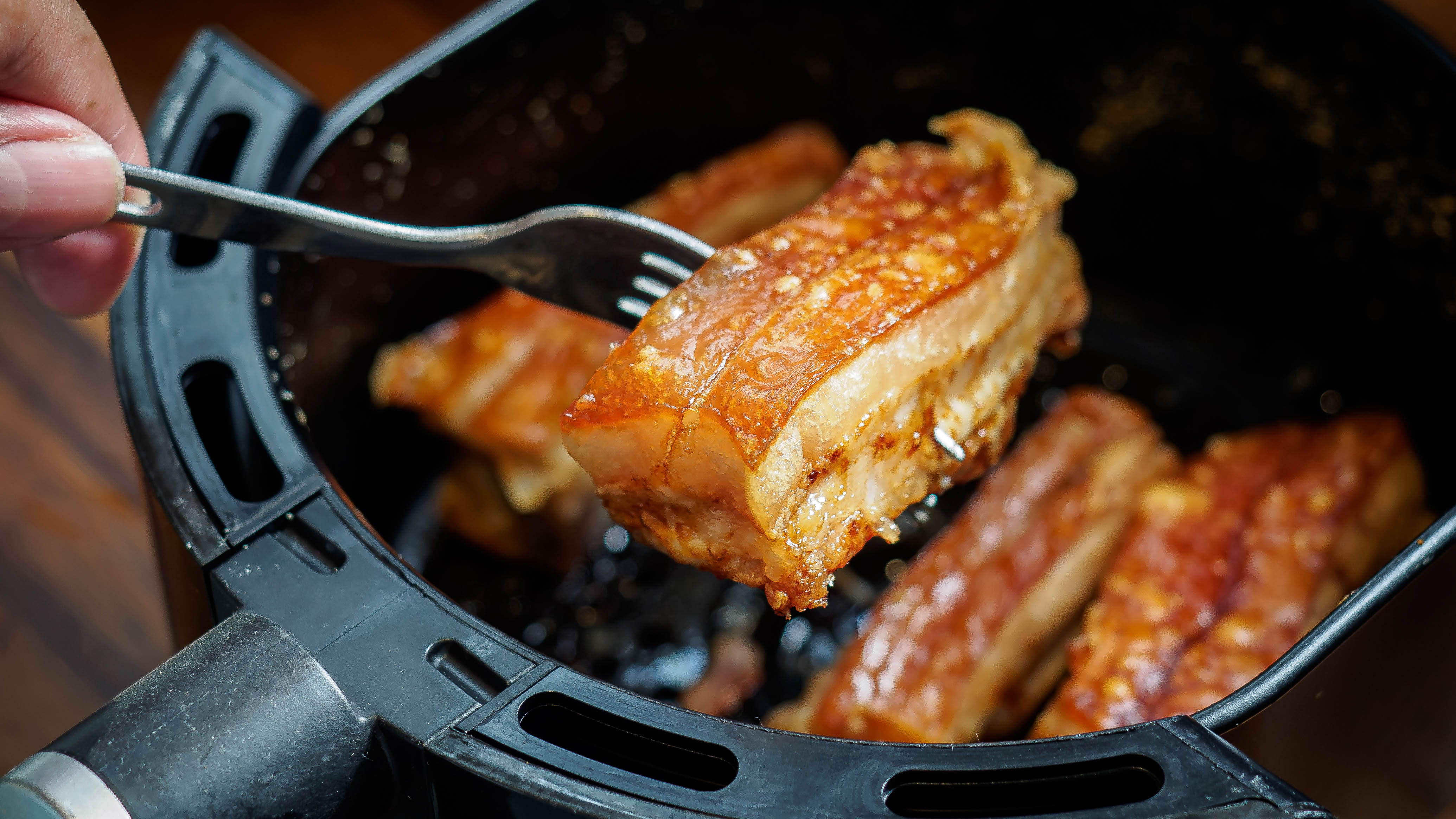 Carne de porco crocante sendo apanhada por um garfo em uma fritadeira