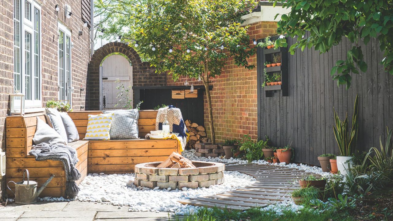 Paved-over garden area with a brick firepit, pallet furniture, and a black painted fence