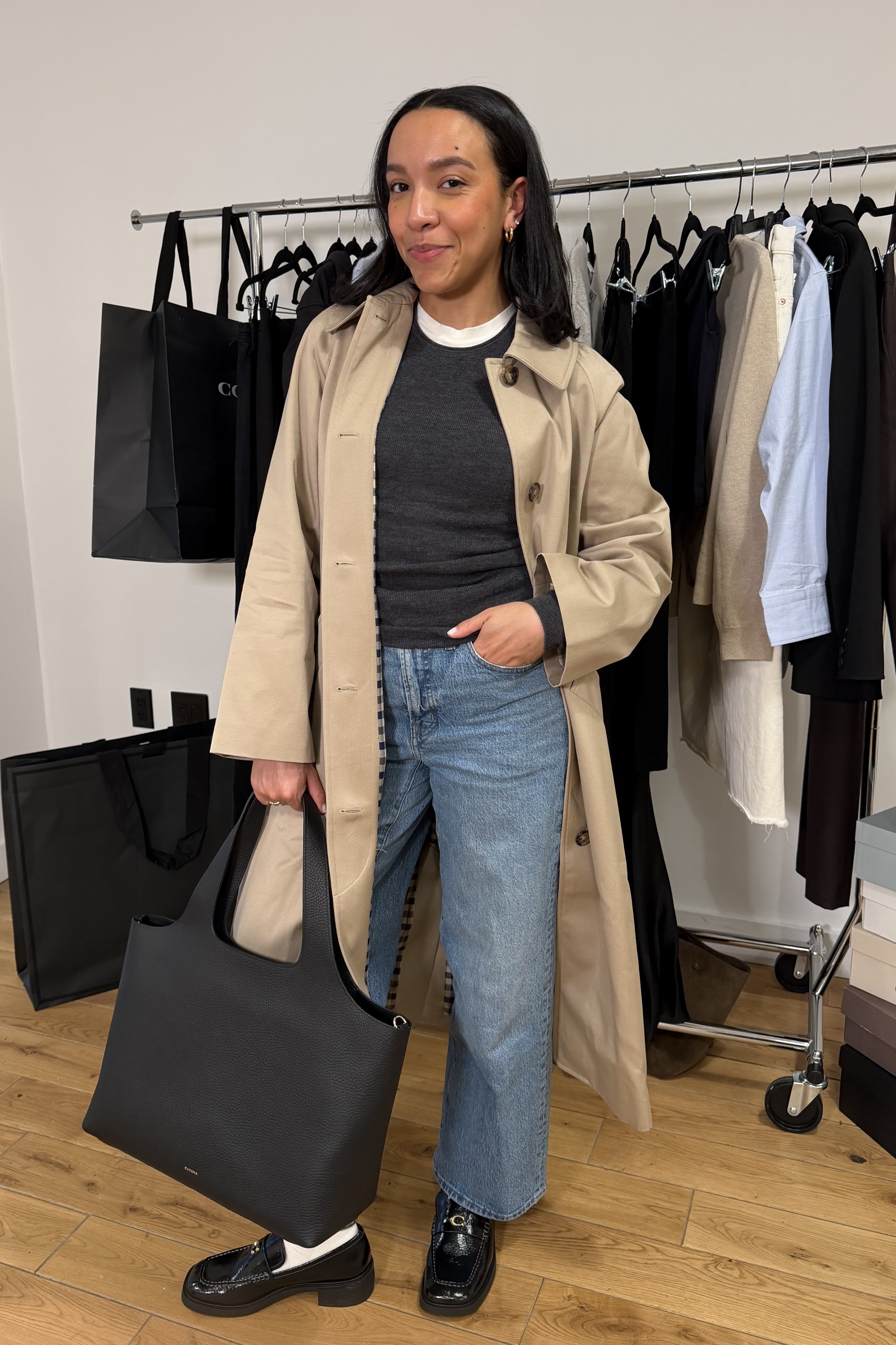 Lauren Tappan wearing a trench coat, a t-shirt, jeans, loafers and socks, and a tote bag