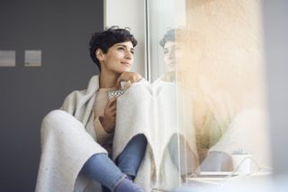 Woman sitting by window, wrapped up in winter