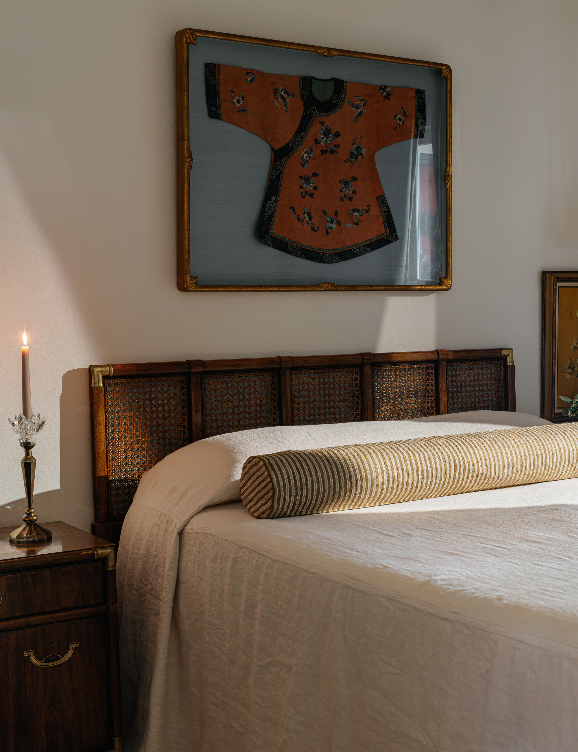 Minimalist bedroom featuring kimono wall art, an antique nightstand, and white bedding paired with an extra long striped bolster pillow