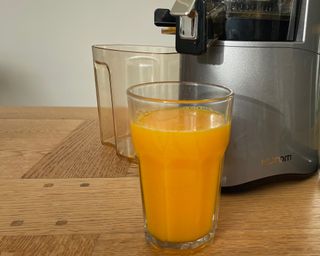 A full glass of freshly-squeezed orange juice prepared using Hurom H-AA slow juicer appliance on wooden dining table