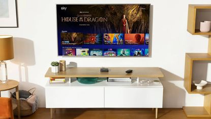 Sky Stream device sitting on TV unit under wall-mounted TV set showing user interface