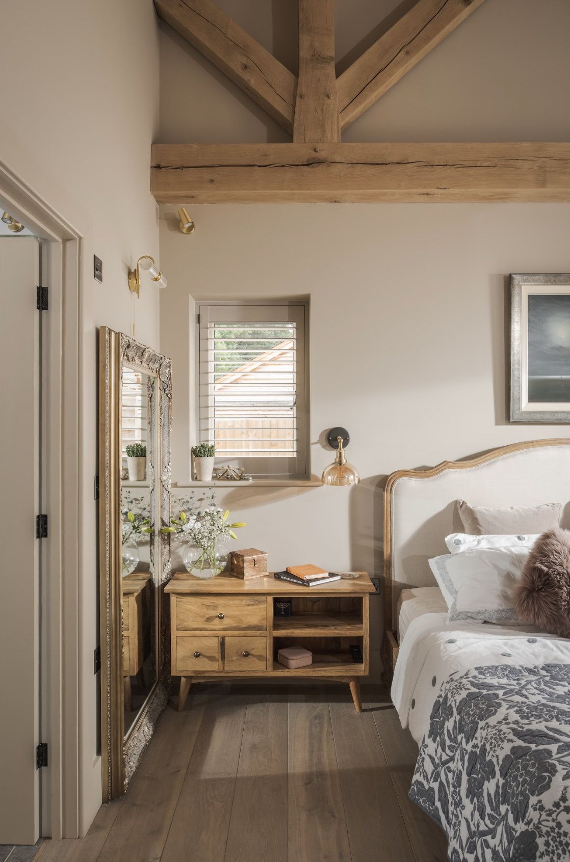 A bedroom with exposed beams, wooden floors, a large wall leaning mirror and a double bed
