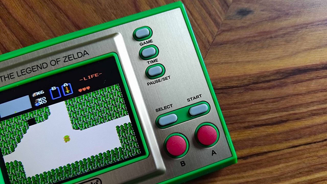 Close up of Zelda Game and Watch B and A action buttons with start, select, pause/set, time, and game toggles above on woodgrain table.