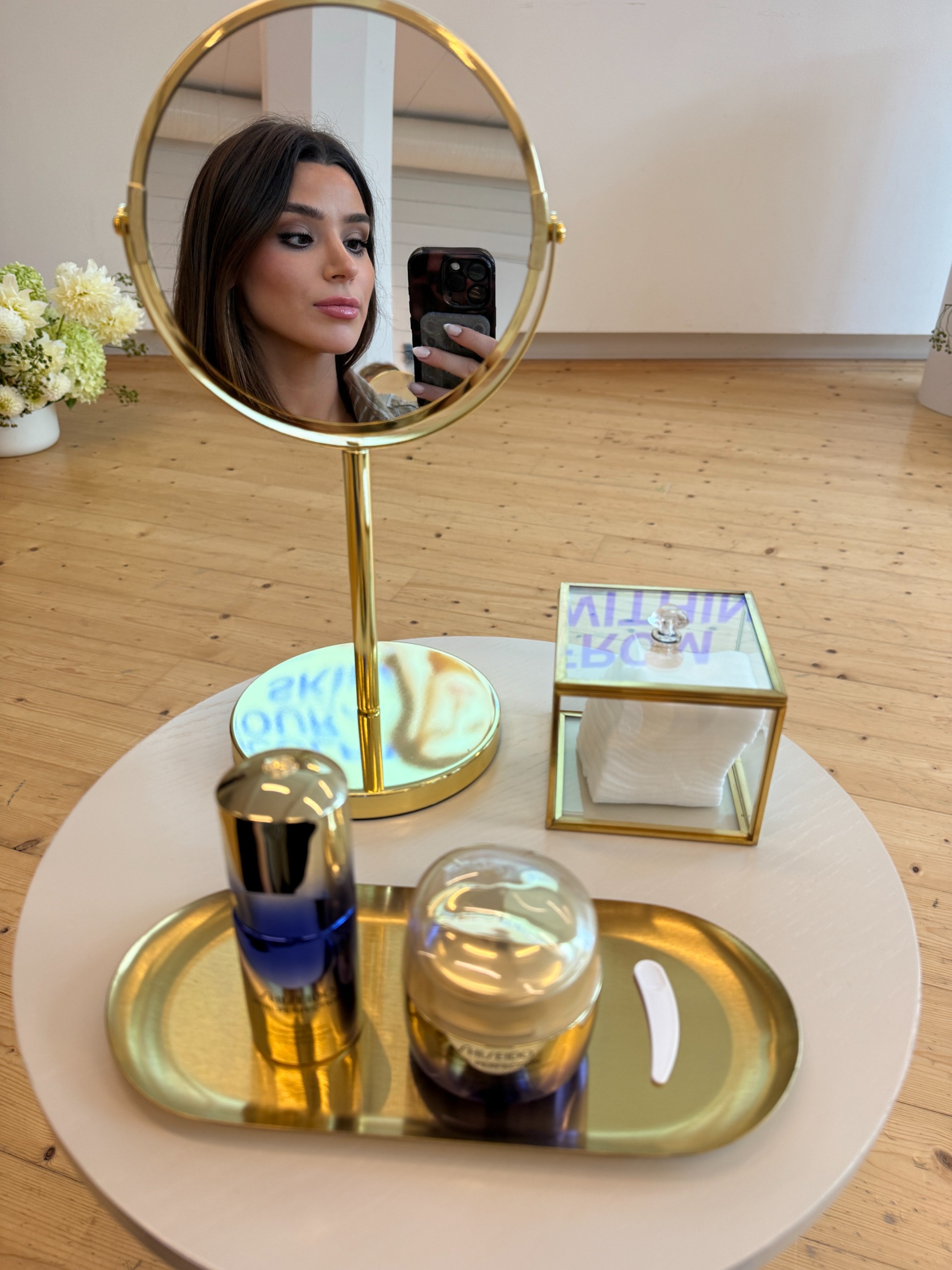 a reflection of a girl in a gold tabletop mirror next to gold skincare accessories and skincare products