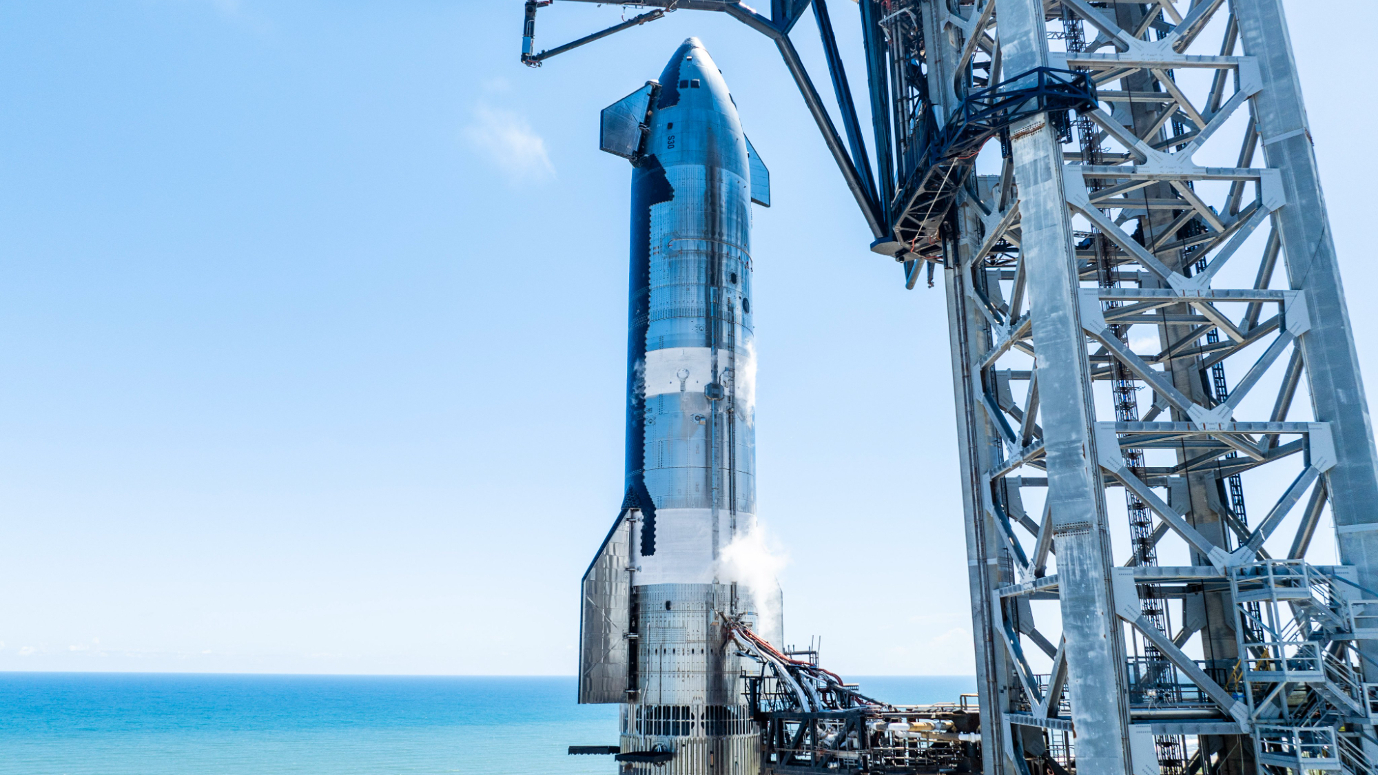 closeup of a silver rocket on a launch pad with the ocean in the background