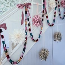 A white staircase with the bannister decorated with velvet ribbon chains, pink bows and paper stars