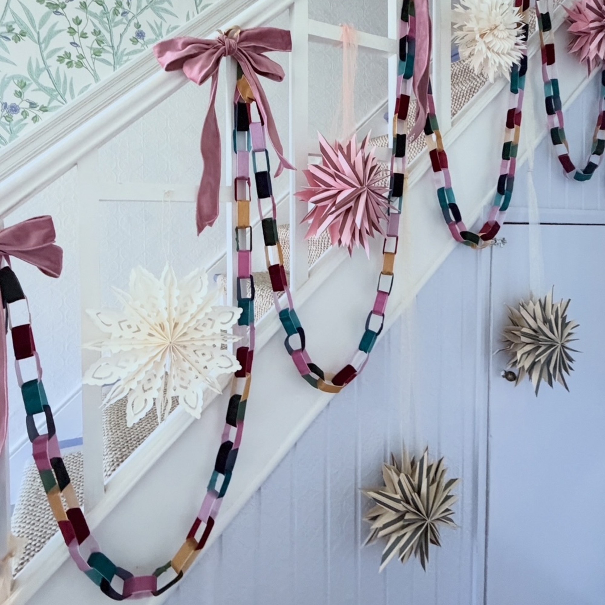 A white staircase with the bannister decorated with velvet ribbon chains, pink bows and paper stars 
