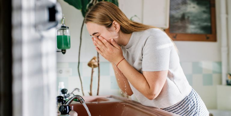 Woman washing her face at a sink