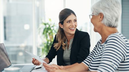 A female professional meets with an older woman. They are going over legal or financial documents for estate planning, retirement planning or other matters.