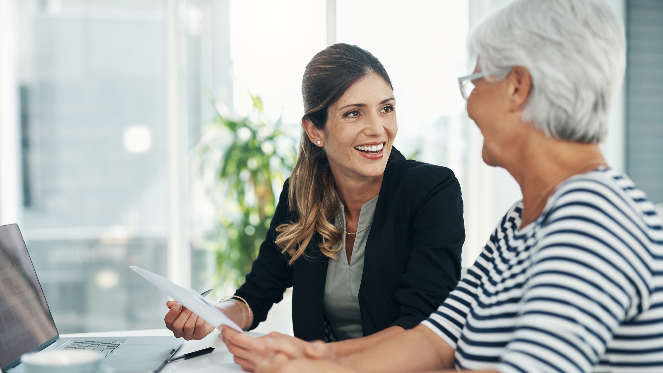 A female professional meets with an older woman. They are going over legal or financial documents for estate planning, retirement planning or other matters.