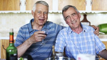 A gay male couple sit at the kitchen table enjoying a bottle of wine.