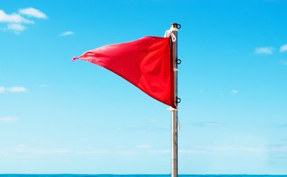 Red warning flag on the beach and turquoise sea on background, red flag meme