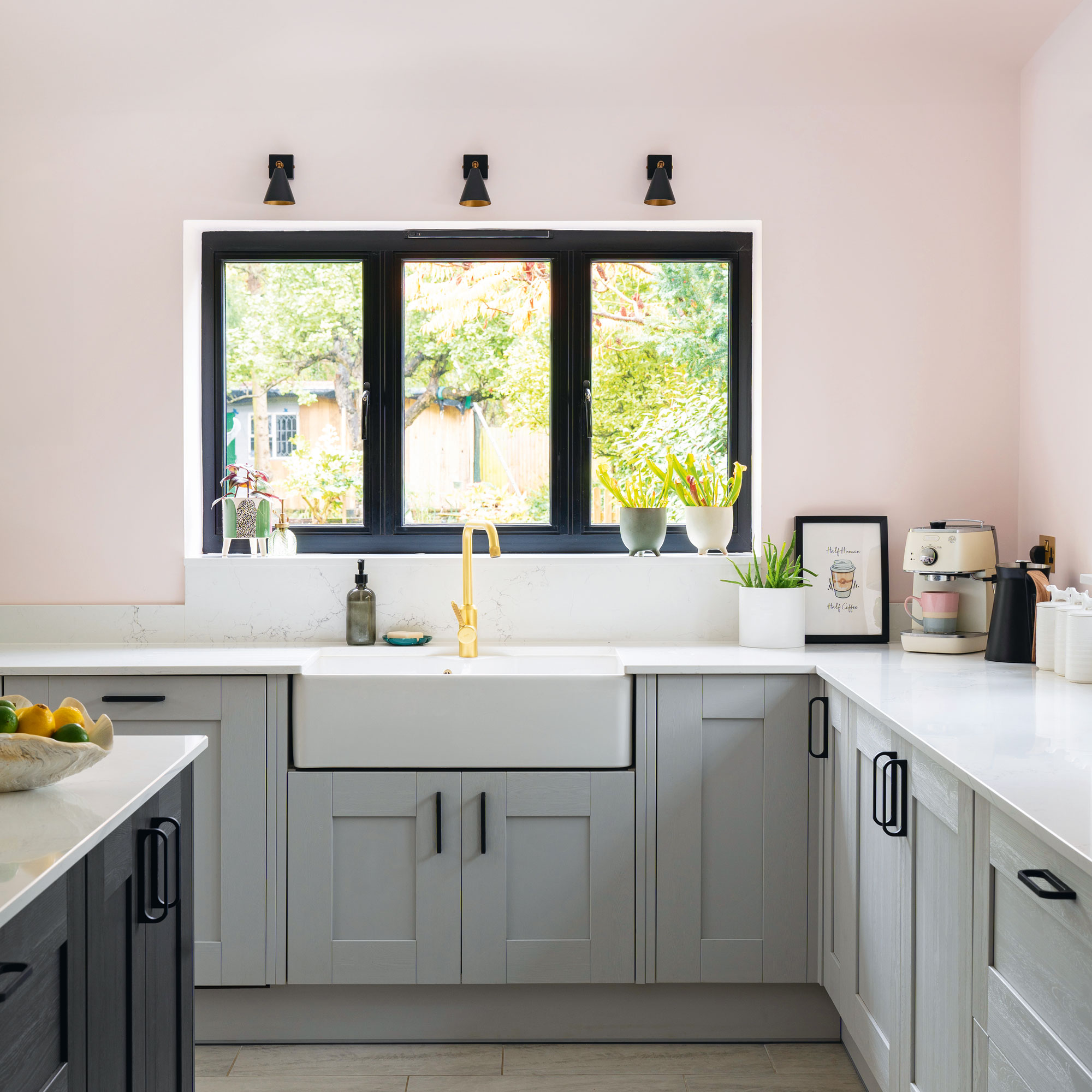 Pink walls and white kitchen worktop with grey cabinets and a kitchen sink under a window