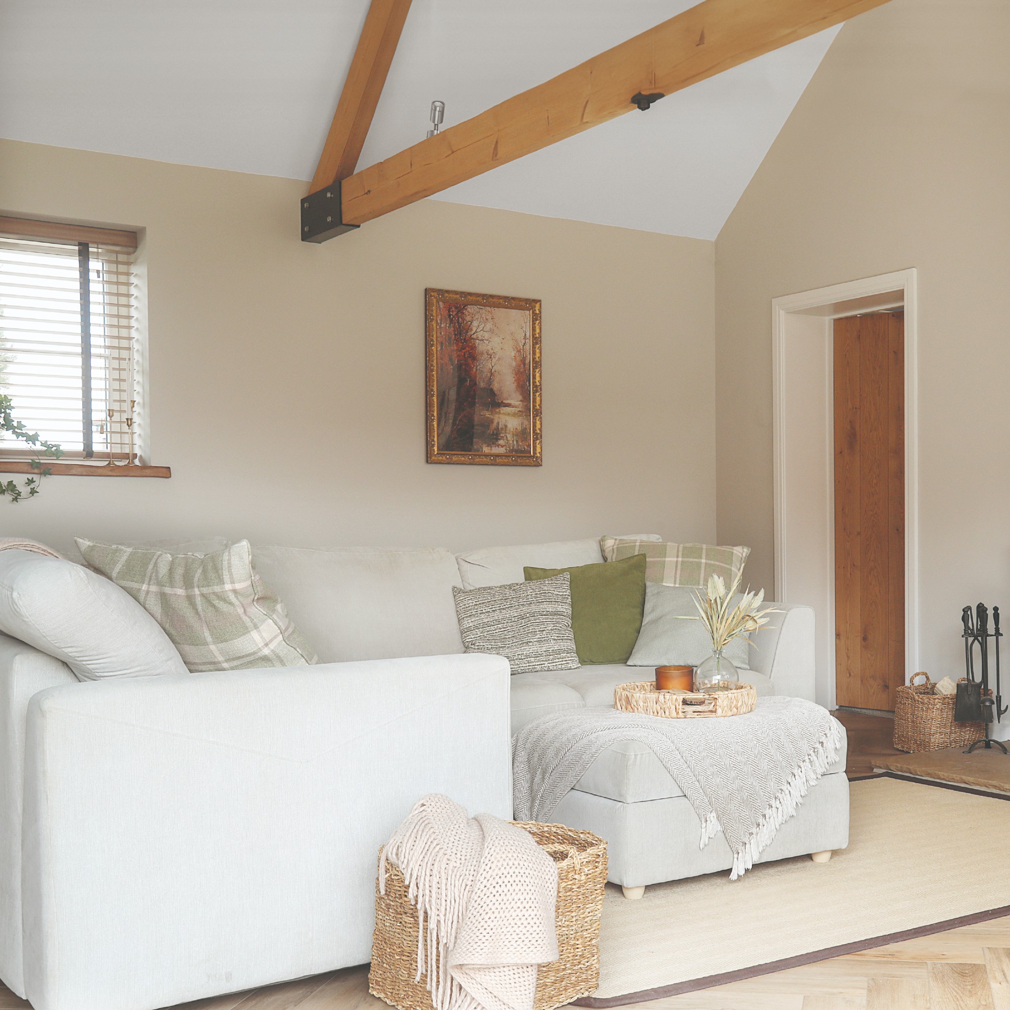 A neutral open-plan living room with a corner off-white sofa and a matching ottoman used as a coffee table